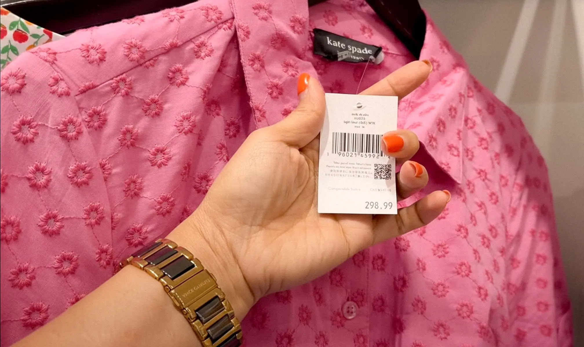 Hand holding a retail price tag over a pink handbag